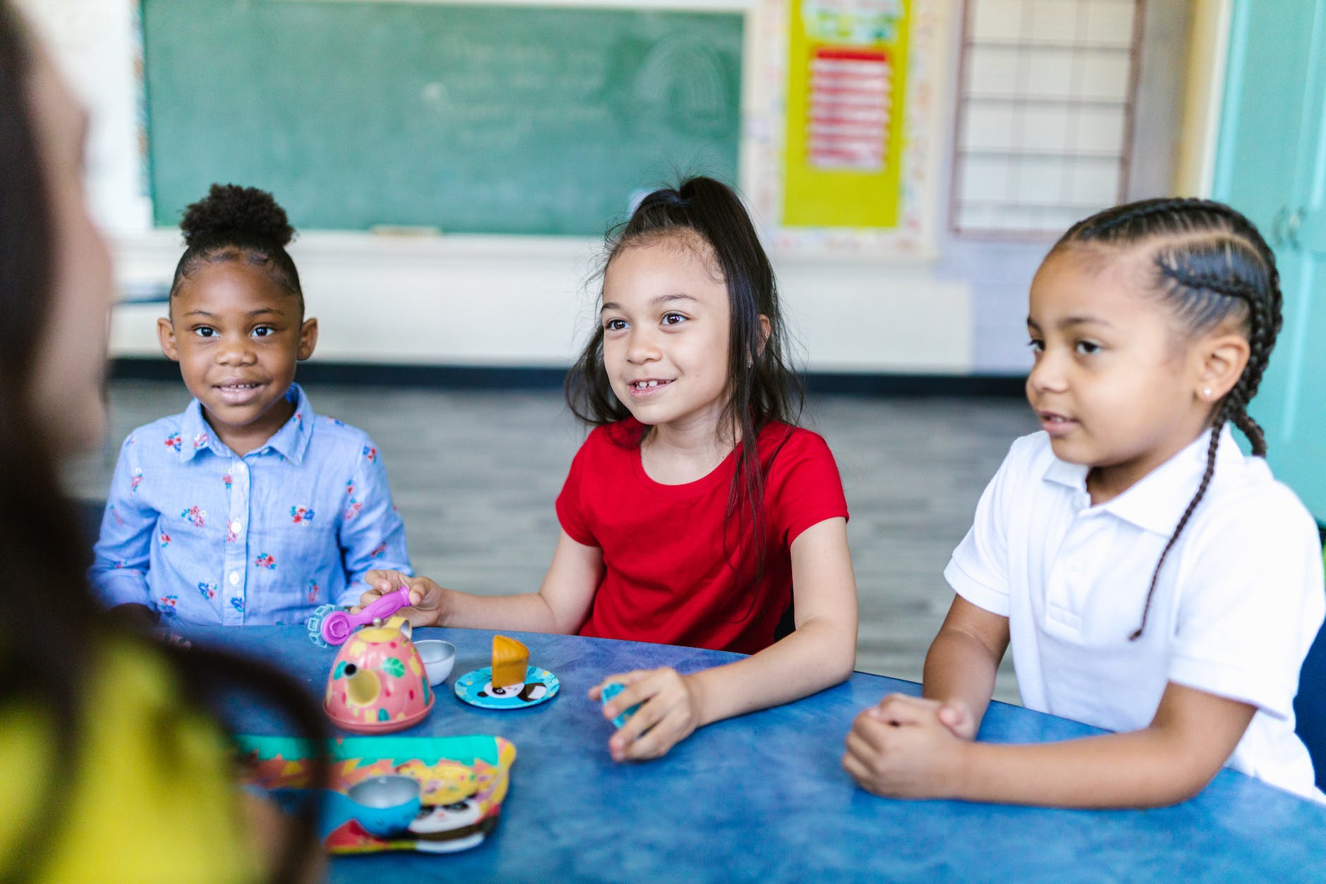 three girls sitting at the table and listening to the teacher in the classroom