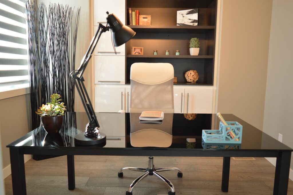 A lamp sits on a desk in a small office. The lamp provides improved lighting for this office.