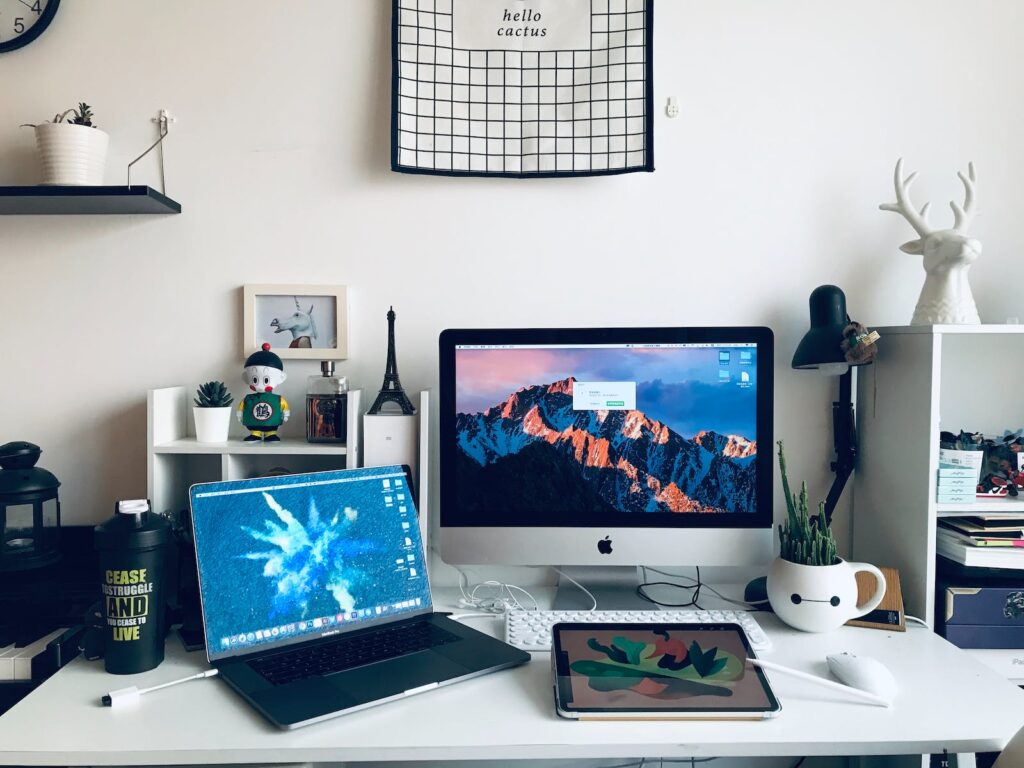 A laptop sits next to a monitor, keyboard, and mouse on a white desk. An additional monitor as displayed will help a busy SLP get ready for teletherapy sessions by improving their workflow.