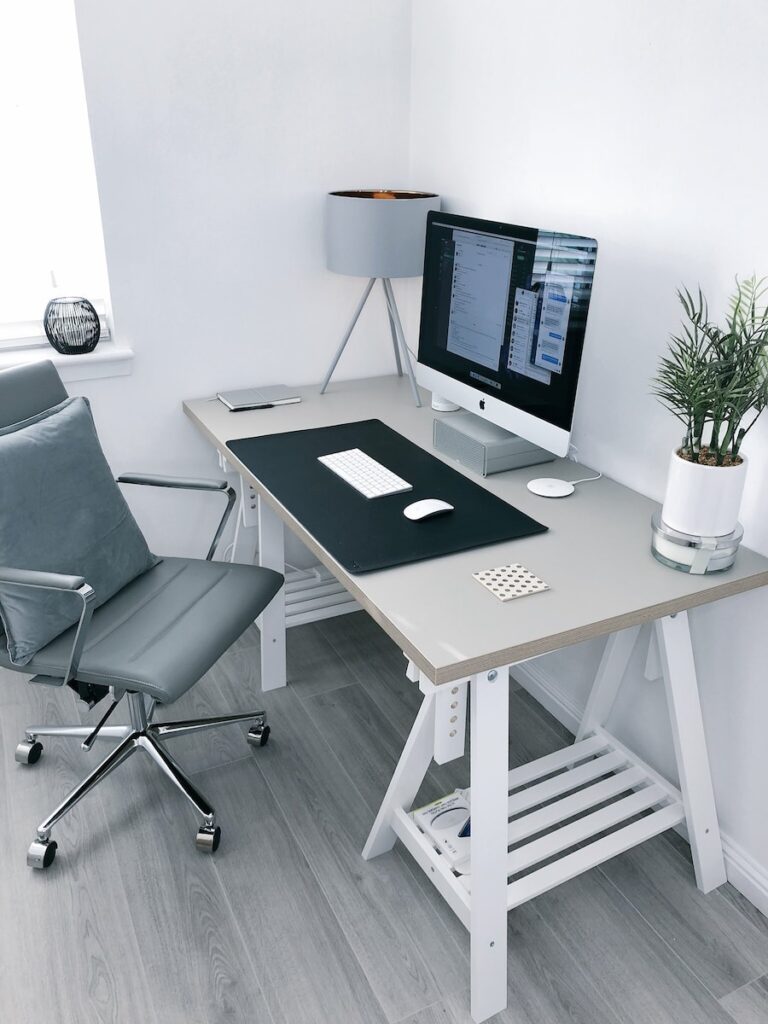 gray leather office rolling armchair beside white wooden computer desk. An organized desk, as displayed here, is important for a speech teletherapy workspace.